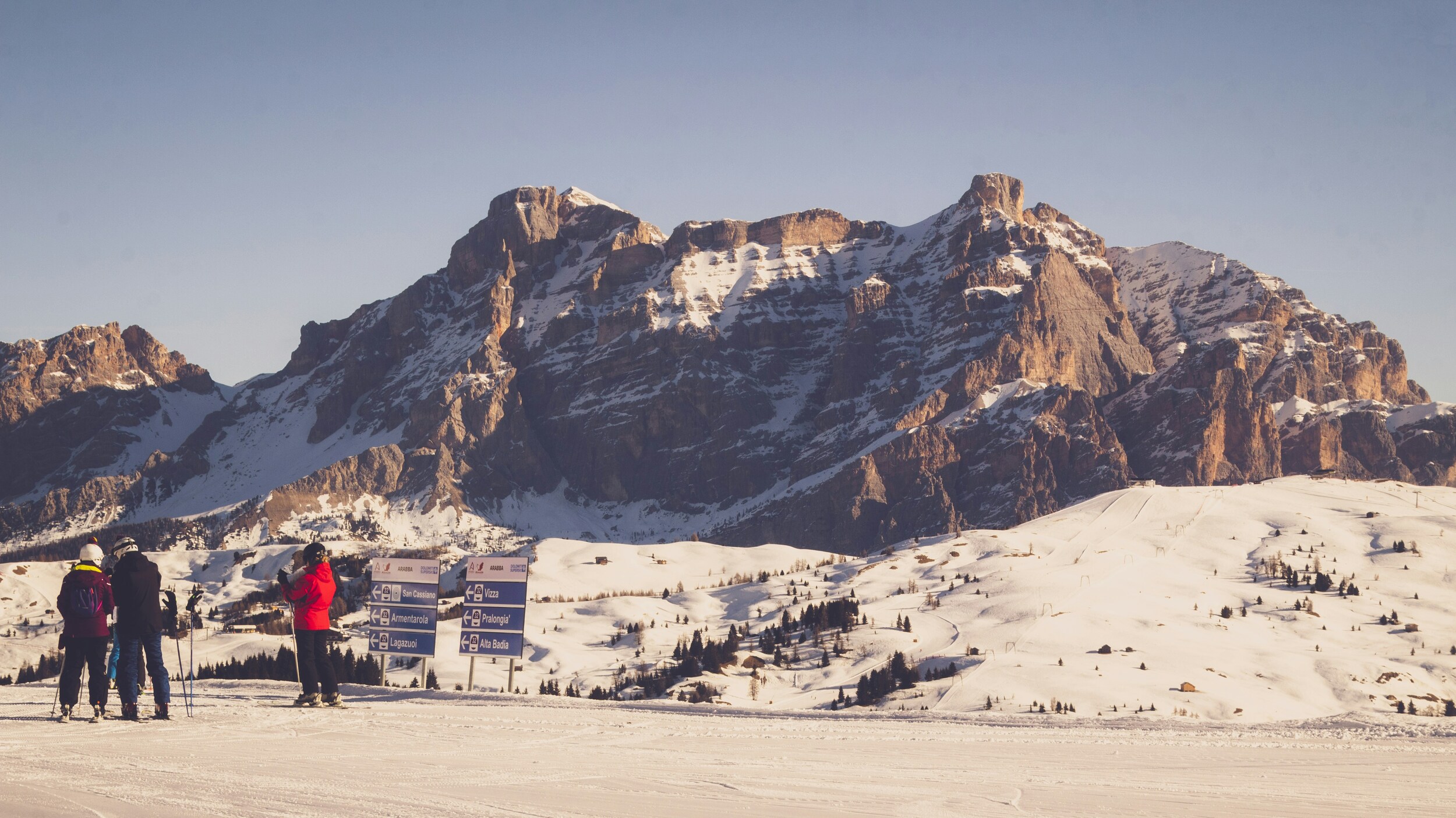 3 skiers on a flat ski slope in front of a mountain massif