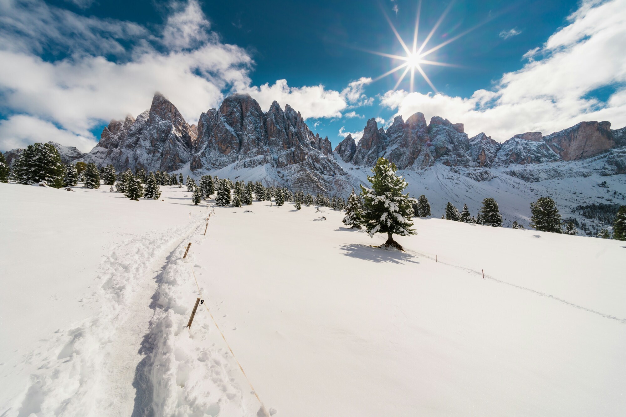 Mountain hiking path in the snow near a fence with clear blue sky