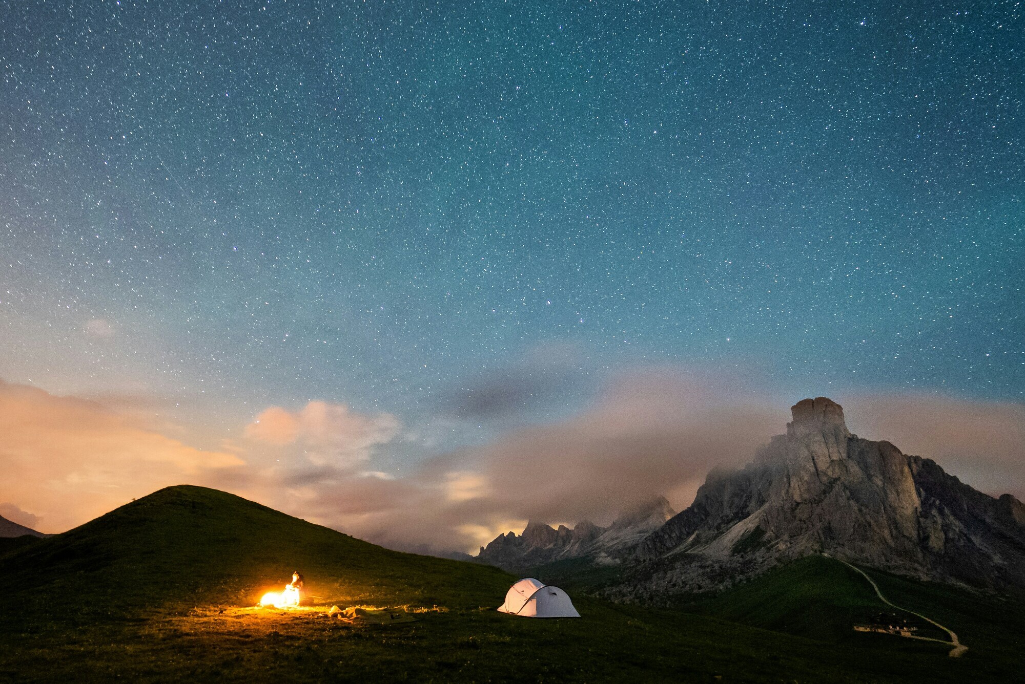 Tend and campfire at night, starry sky and mountains