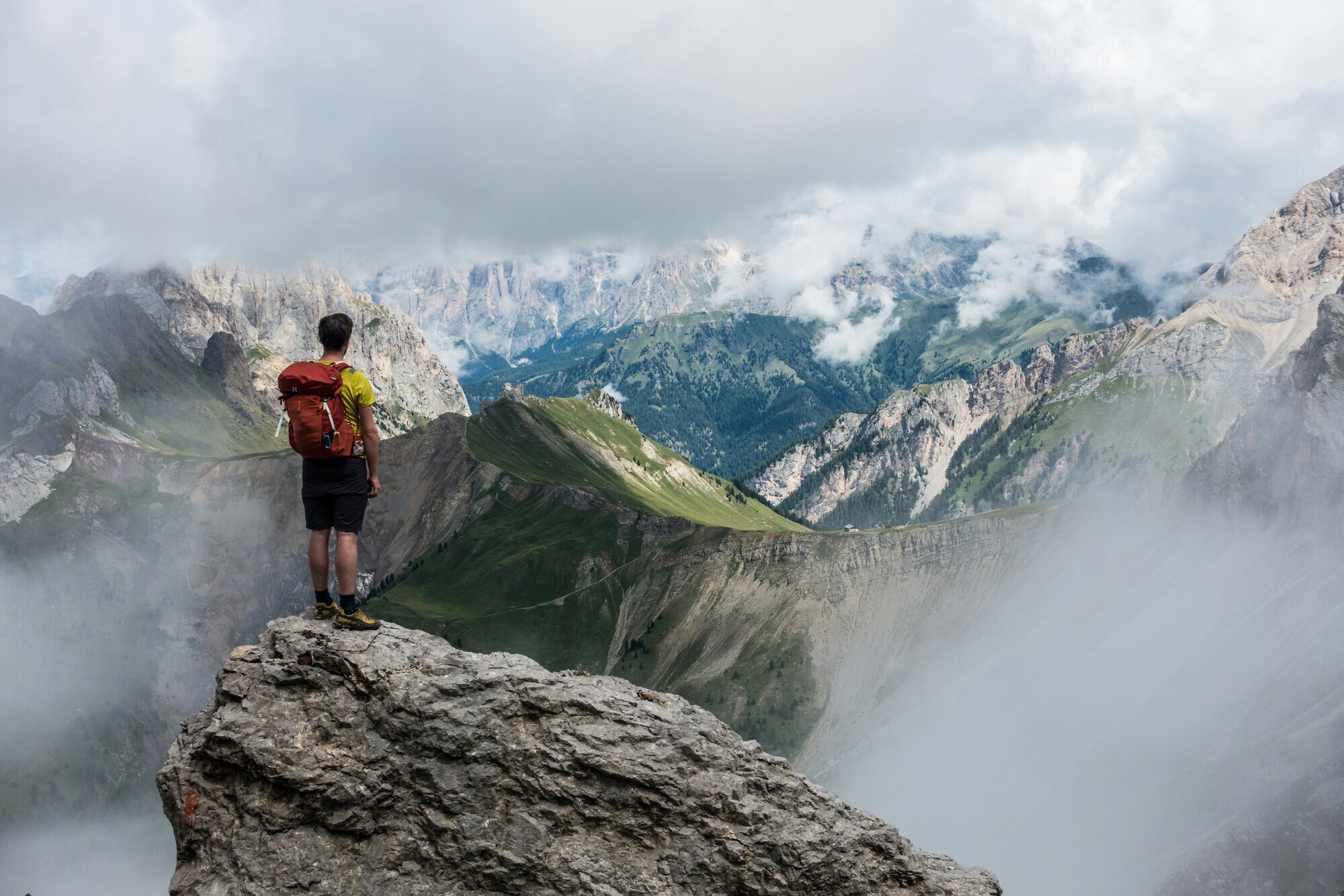 Hiker with backpack on a mountain top observing the foggy peaks and meadows